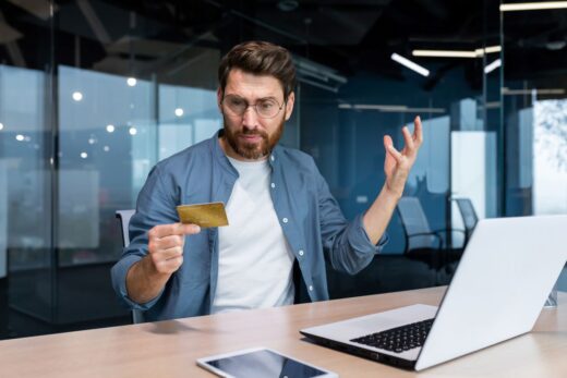 homme contrarié devant son ordinateur avec sa carte bancaire
